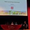 The image shows several people seated on a stage in the Temple Ambler auditorium, participating in a panel discussion about multi-use energy landscapes. The panelists appear to be engaged in conversation, with the audience not visible in the image.