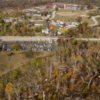 An aerial, overhead view shows the Temple Ambler campus from above, with buildings and open green areas spread across the landscape. In the lower area of the image is the Temple Forest Observatory, where many trees are lying on the ground as a result of the 2021 tornado.