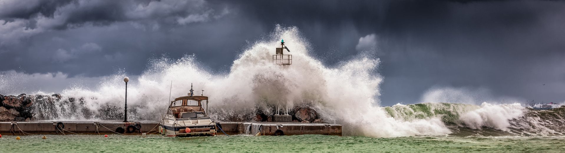 a wave crashing over a boat moored near a barrier