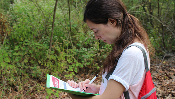a woman doing fieldwork on papers in her hand while in the woods