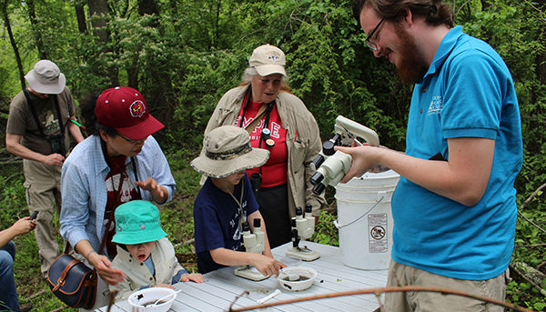 Kids and adult engaging in citizen science by looking at samples through microscopes.