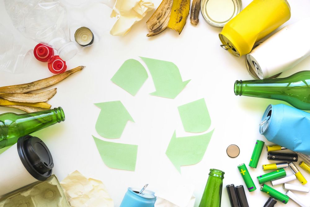 the recycle symbol, three arrows chasing one another, surrounded by items than can be recycled like glass bottles and plastic